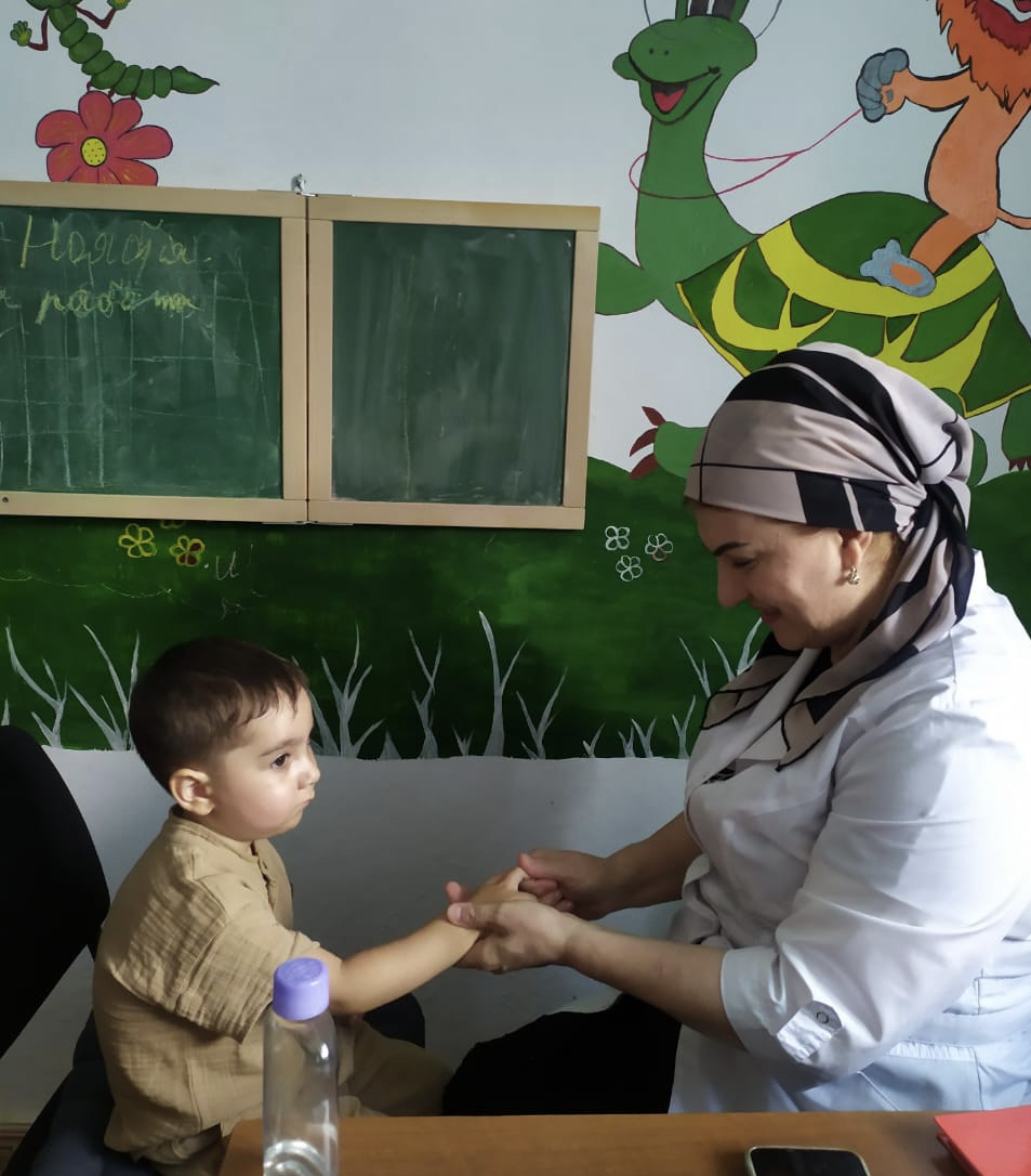 Воспитатель Джамавова Барият проводит пальчиковый массаж подопечному Центра.